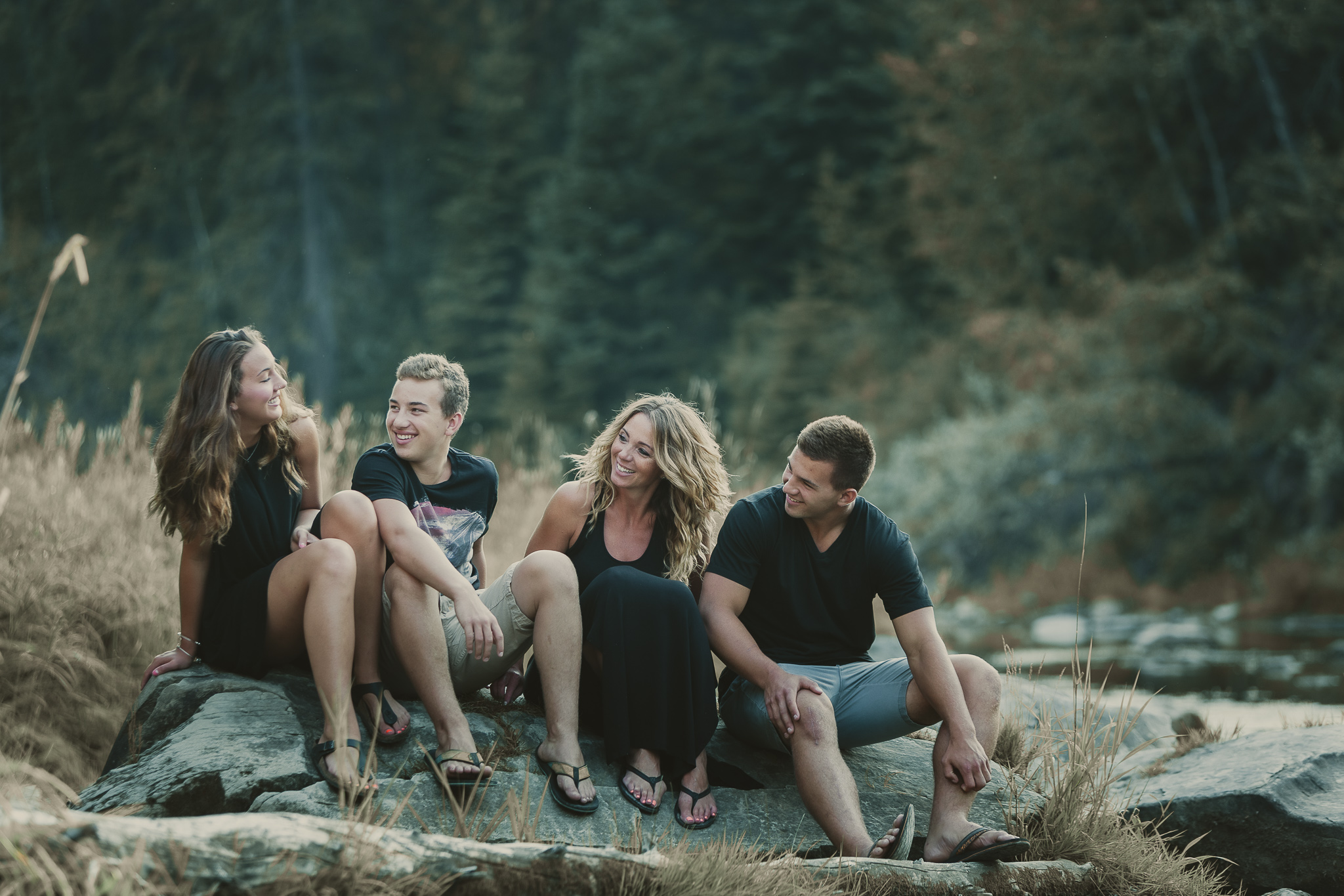 four people sitting on a rock and laughing