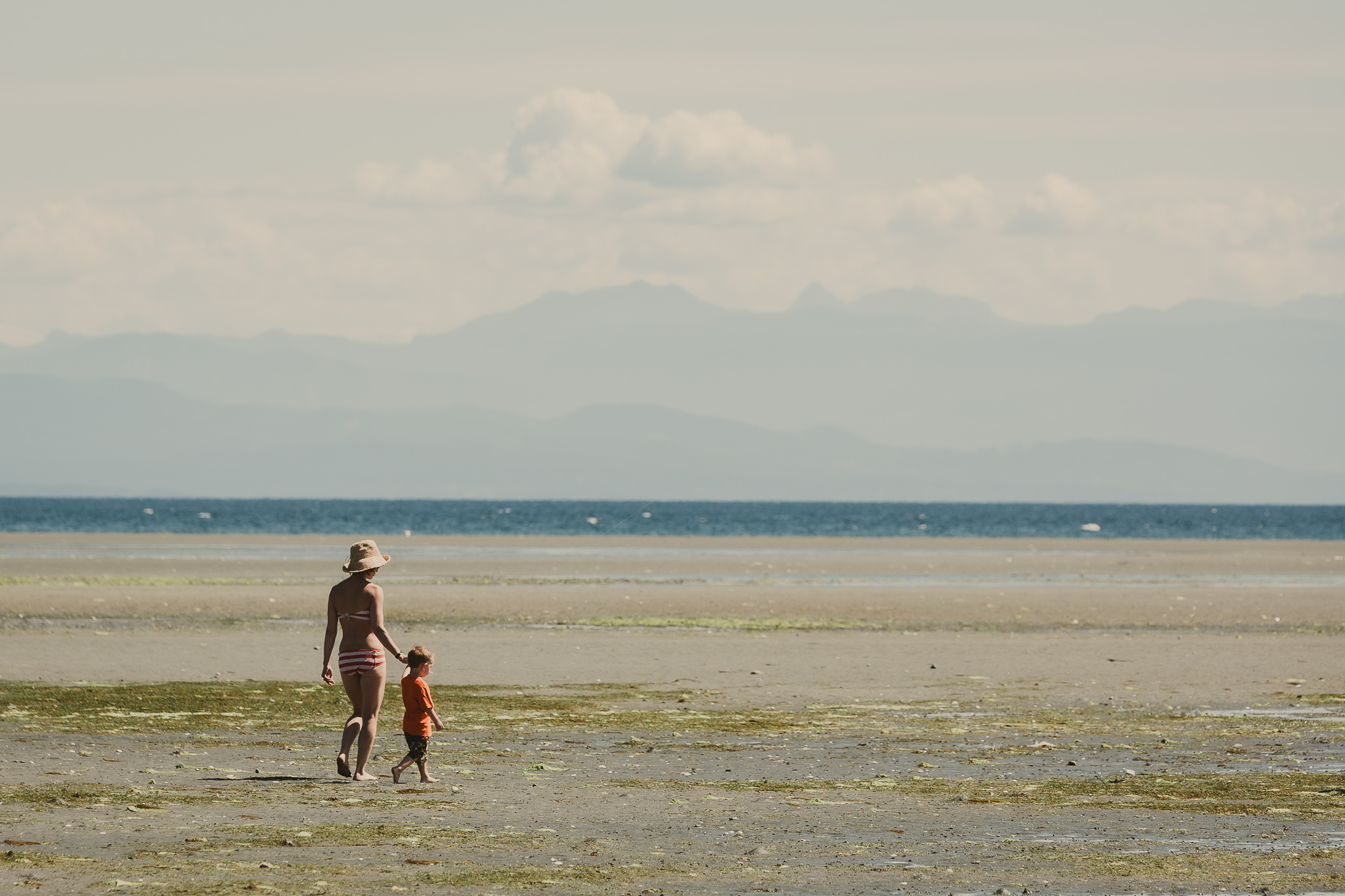 woman and small child walking on sand near ocean