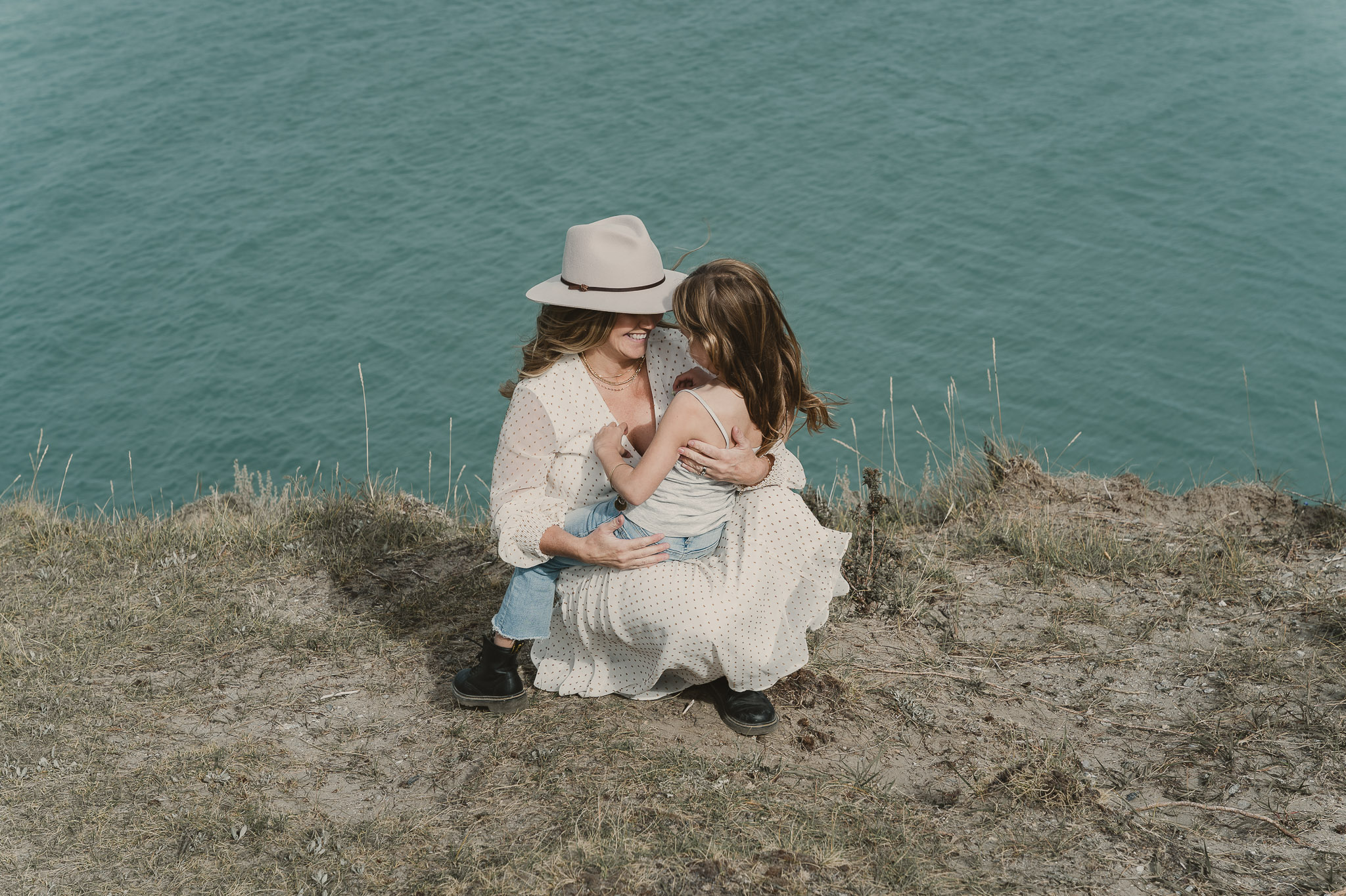 woman knelling on ground holding small girl by blue lake