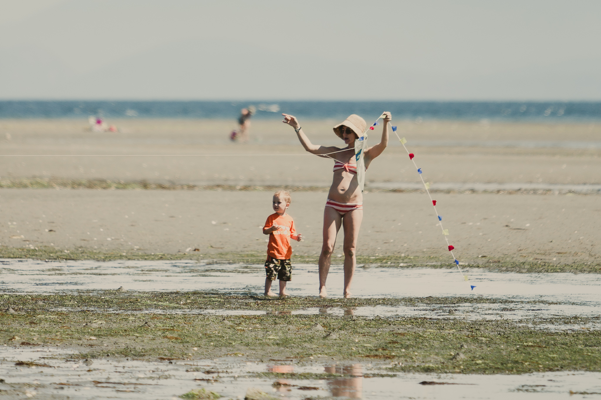 woman in bathing suit flying kite with small child