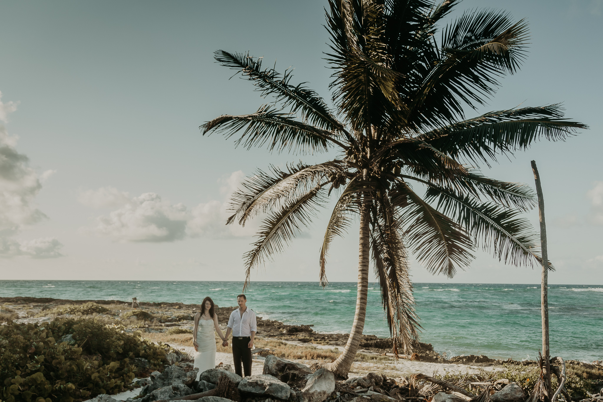 wedding couple holding hands under a palm tree
