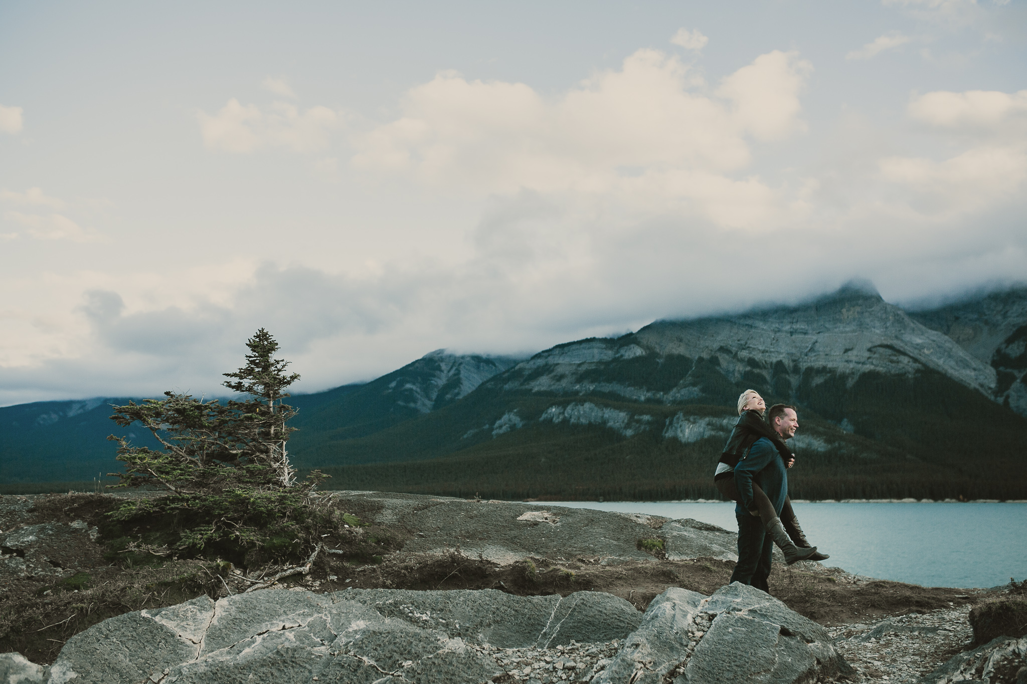 man piggybacking woman by a blue lake in the mountains