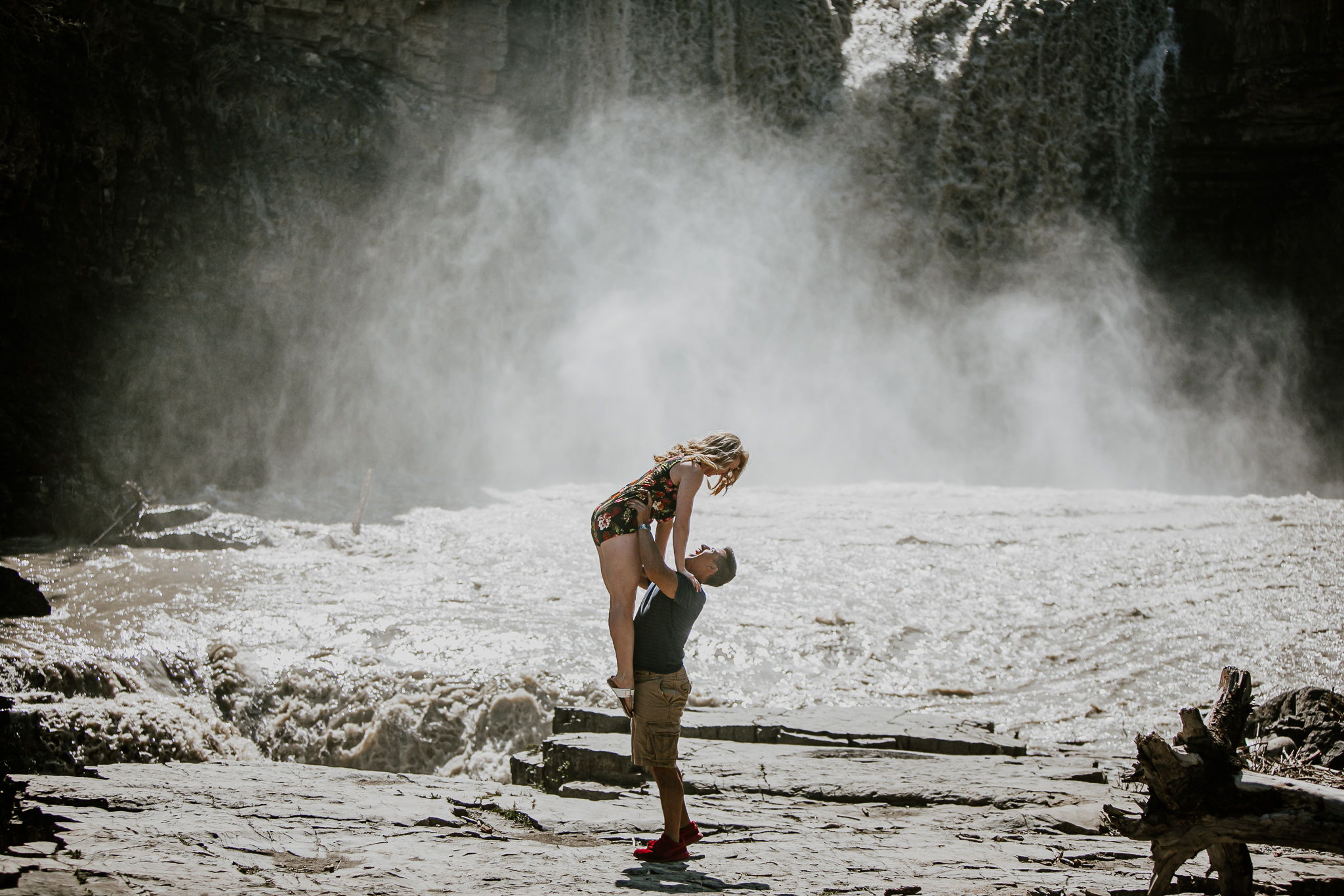 man holding woman over head by a waterfall