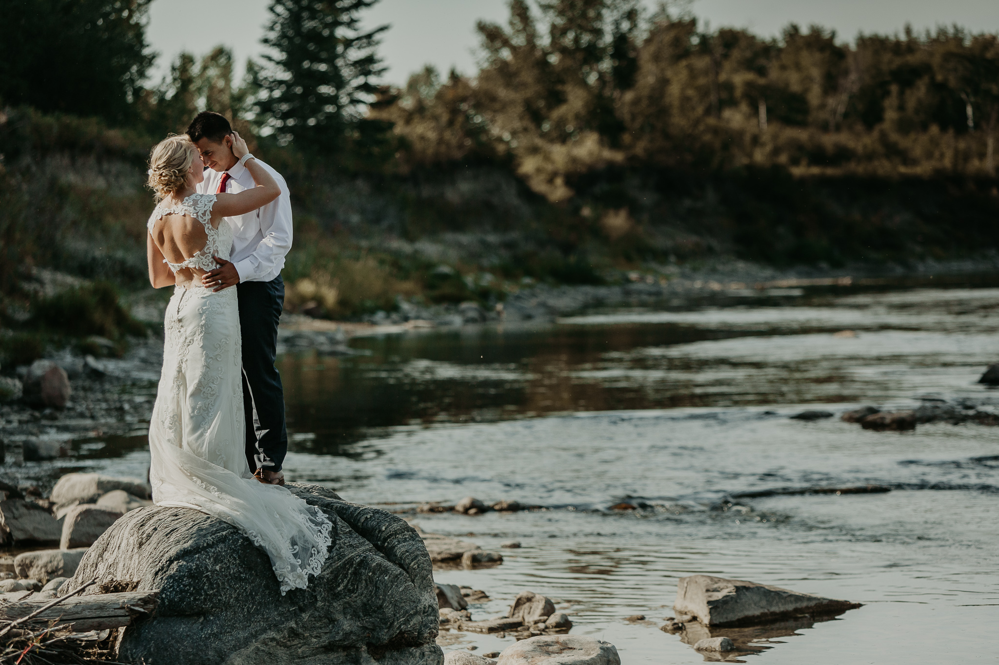bride and groom standing on a rock in the river