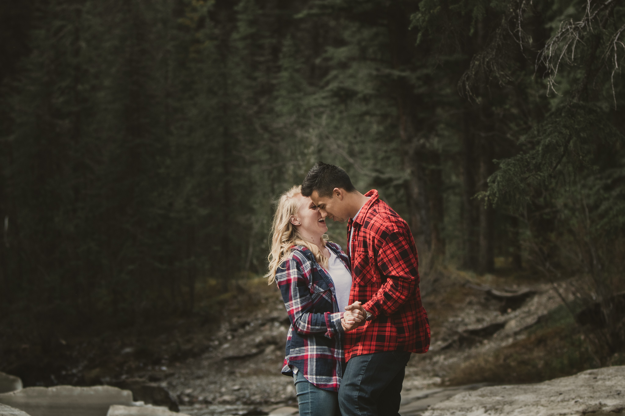 man and woman in plaid flannel dance on a rock in the river