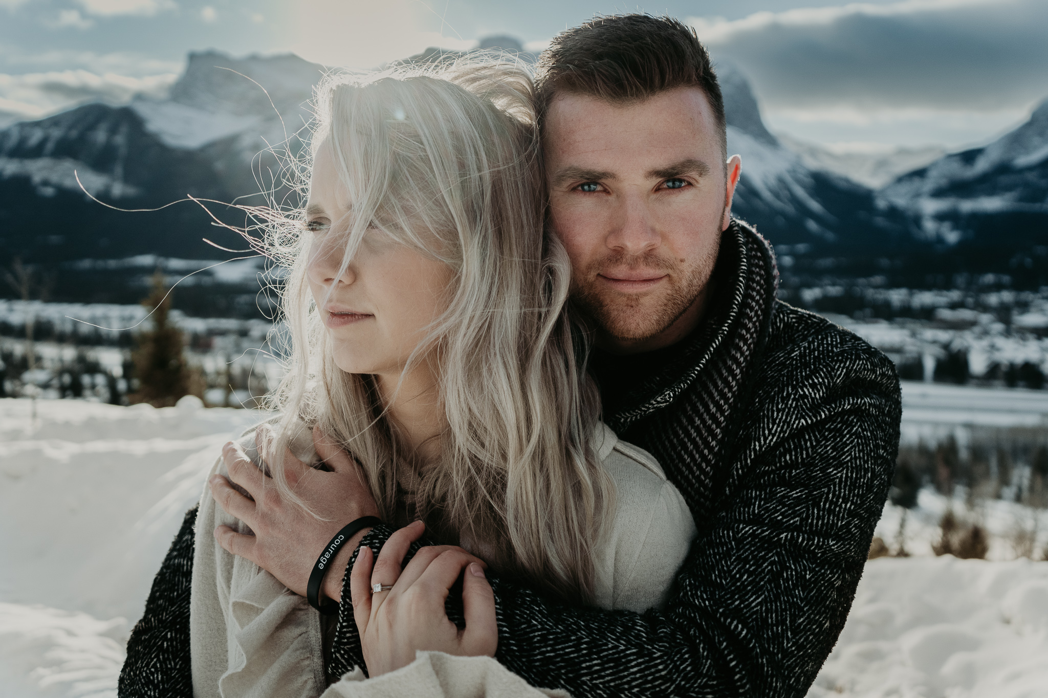 man holds blond woman from behind in the mountains