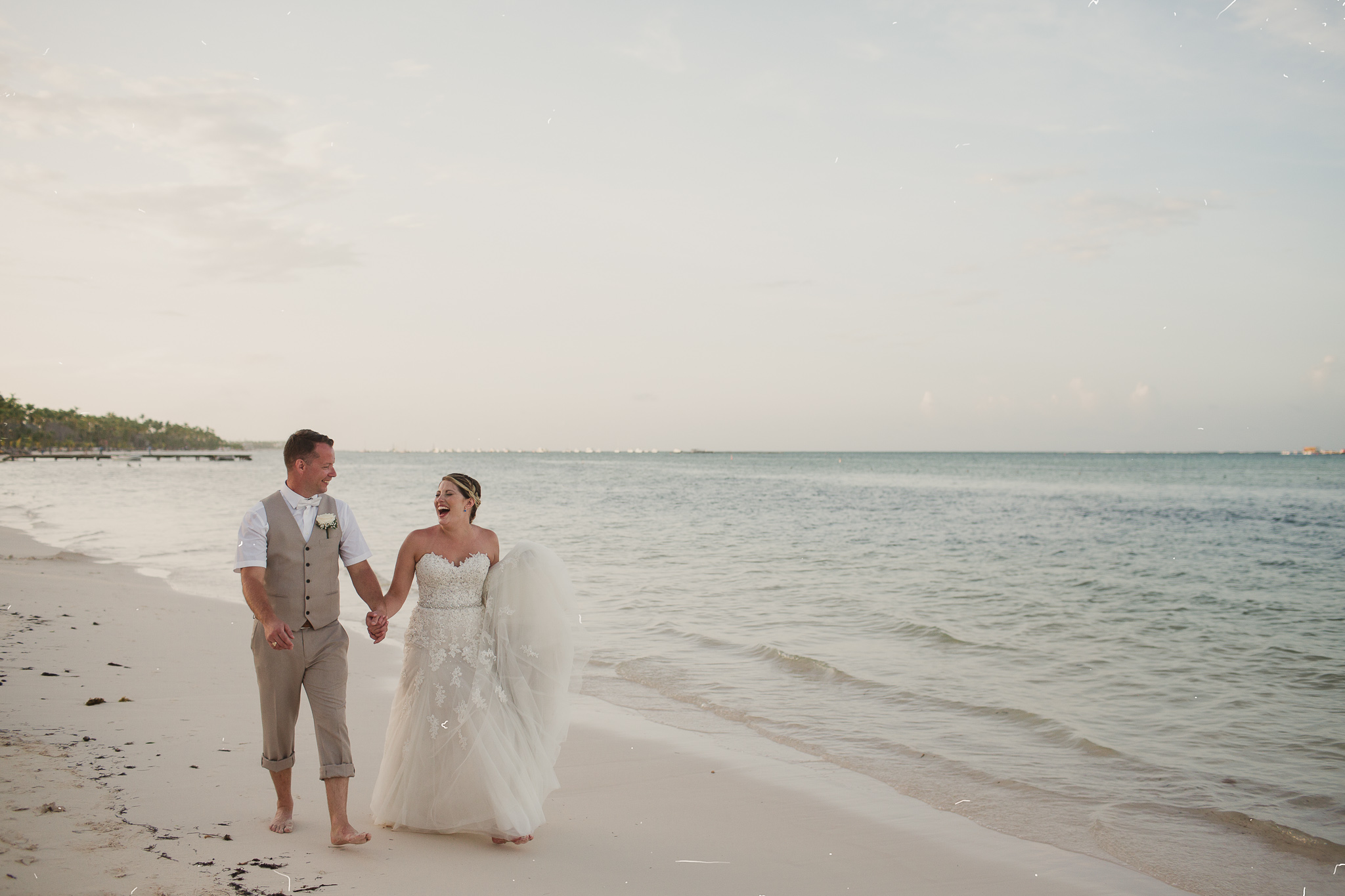 man with woman in a wedding dress walking on the beach