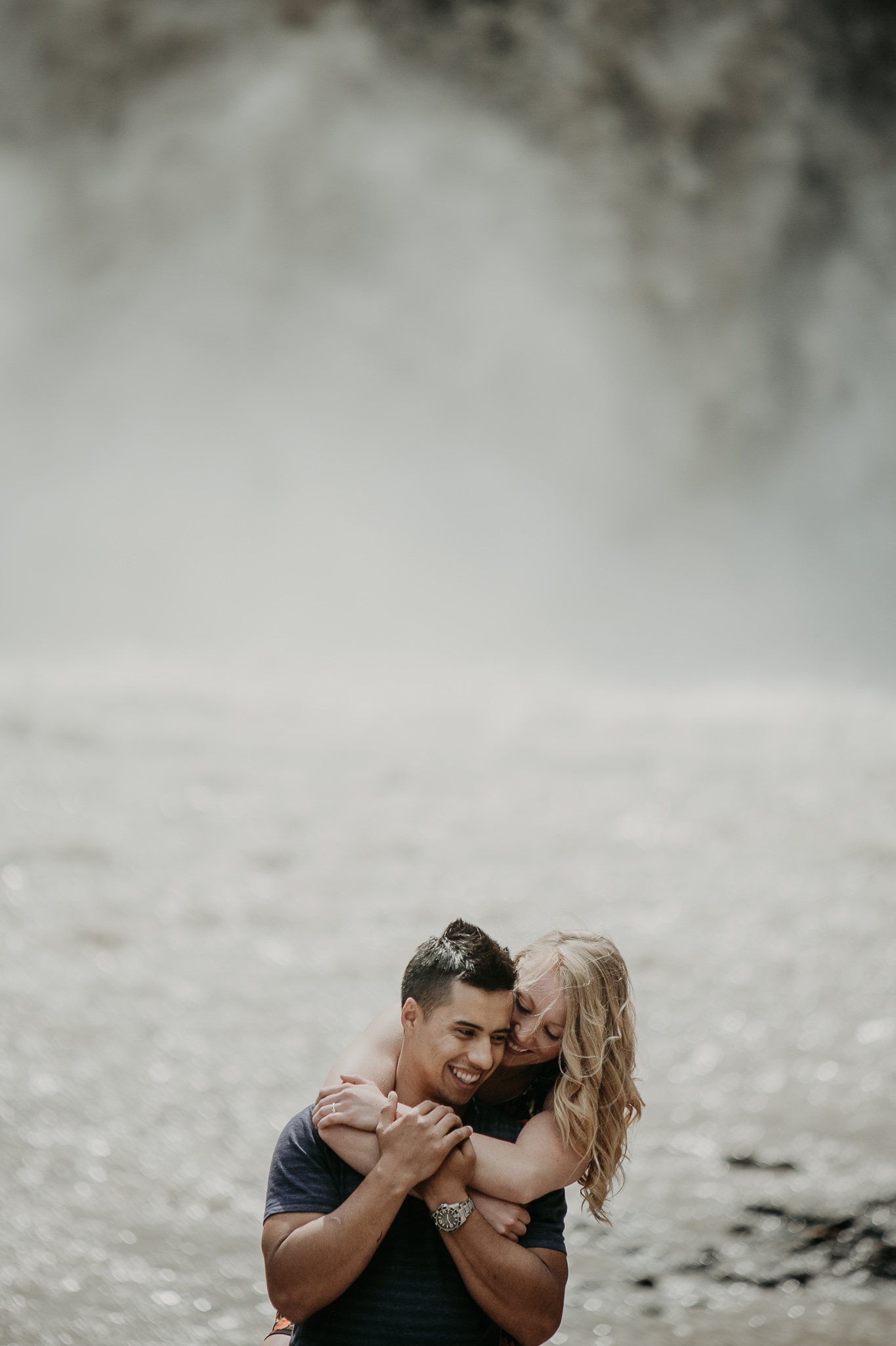 woman hugs man from behind near waterfall