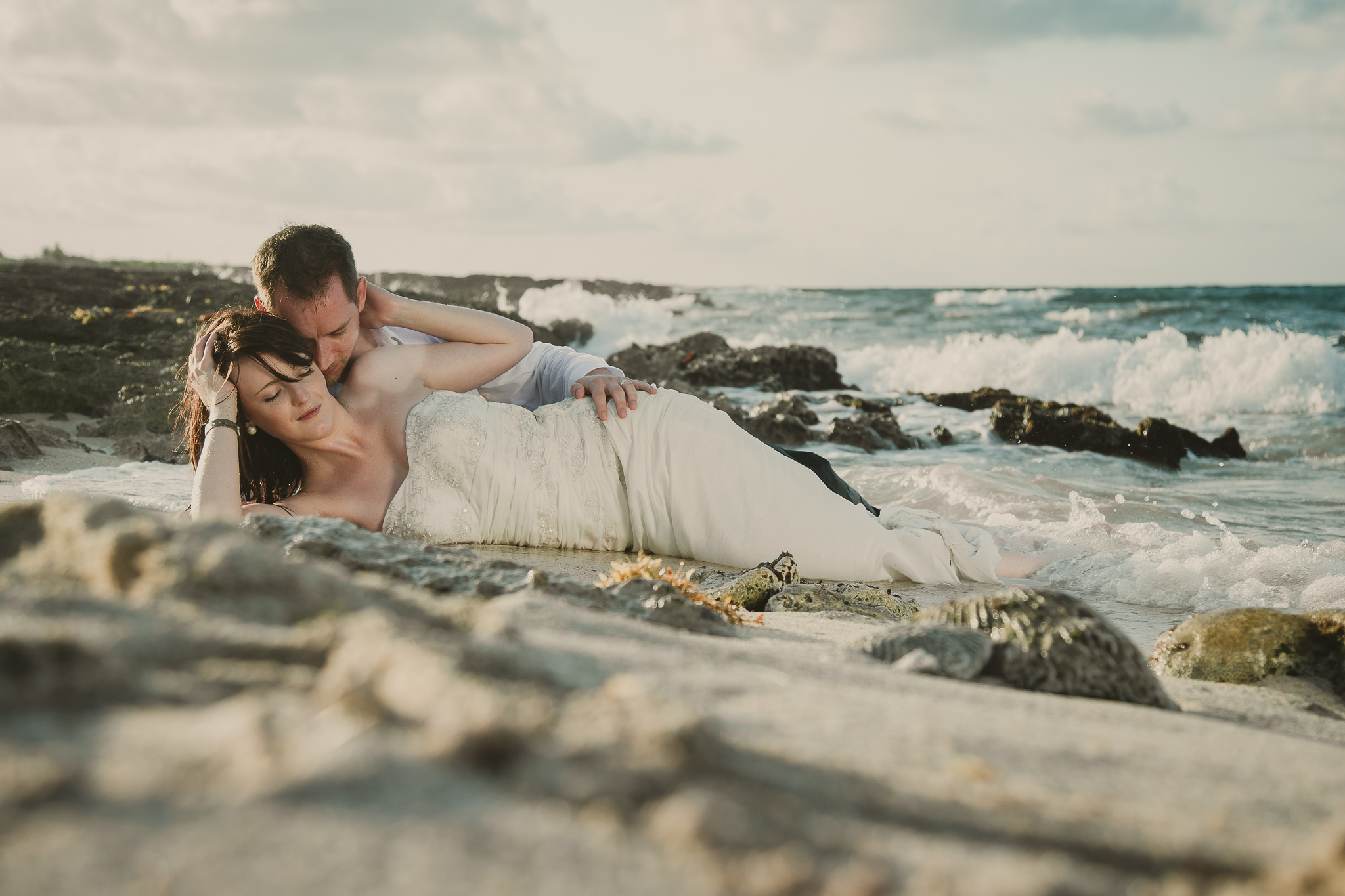 man and woman laying in the sand and waves splashing up