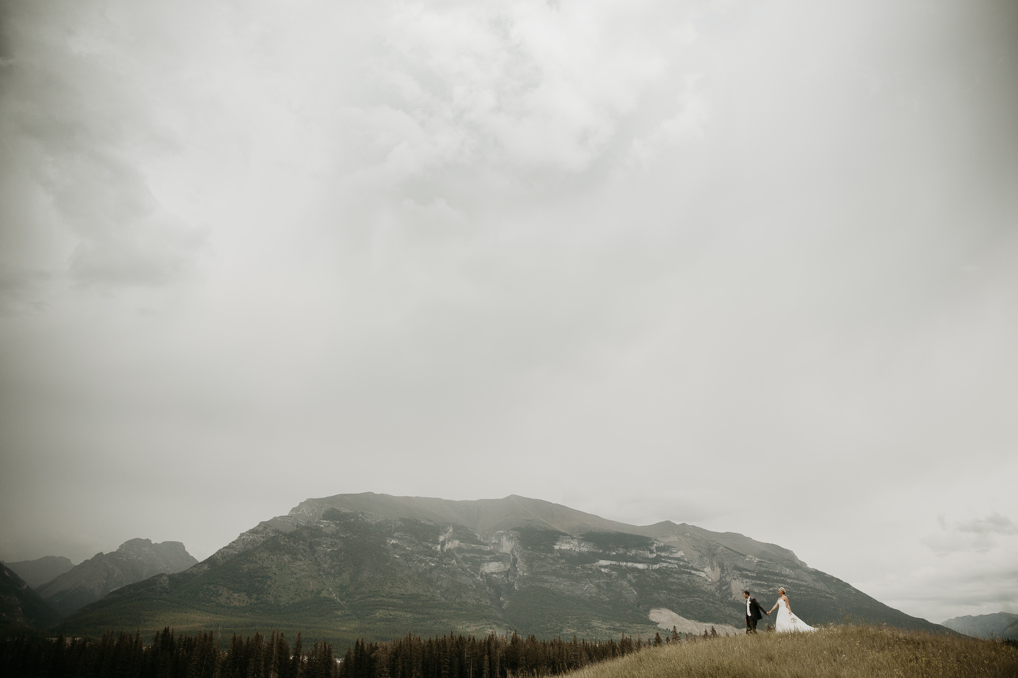 man and woman in a long white dress walking in the mountains