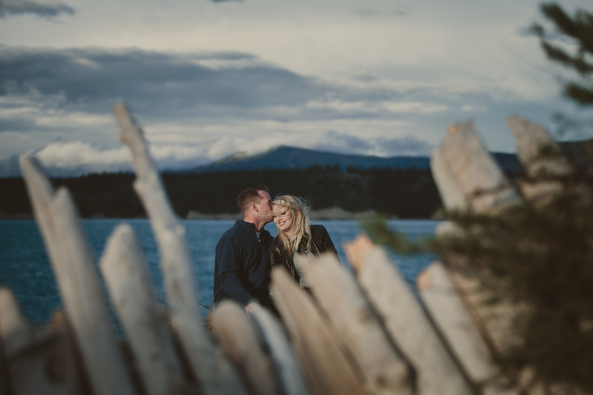 man kisses woman's temple behind fence by a blue lake