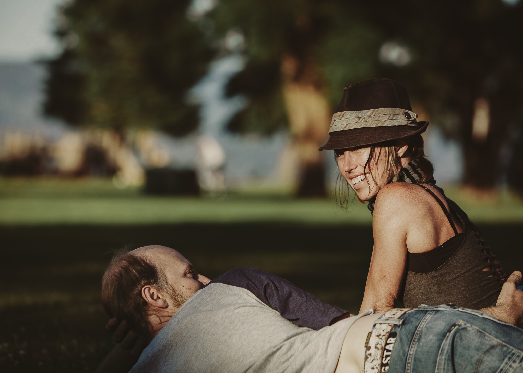 man lays on grass beside smiling woman with hat on