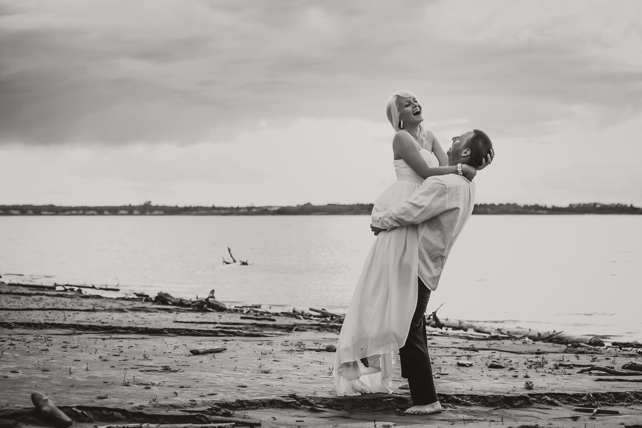 man picks woman in long white dress up at the beach