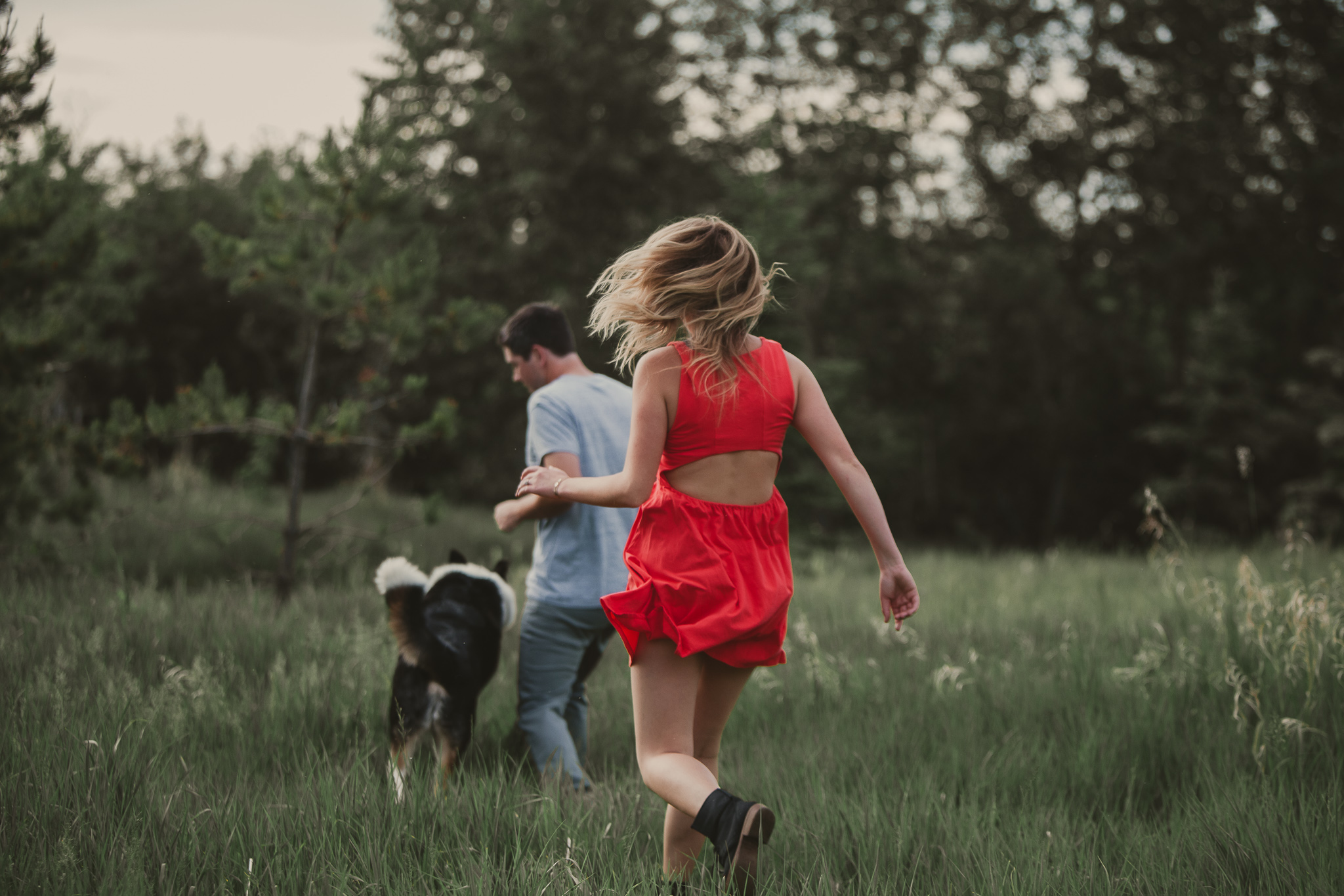 woman in red dress chases man and dog in the grass