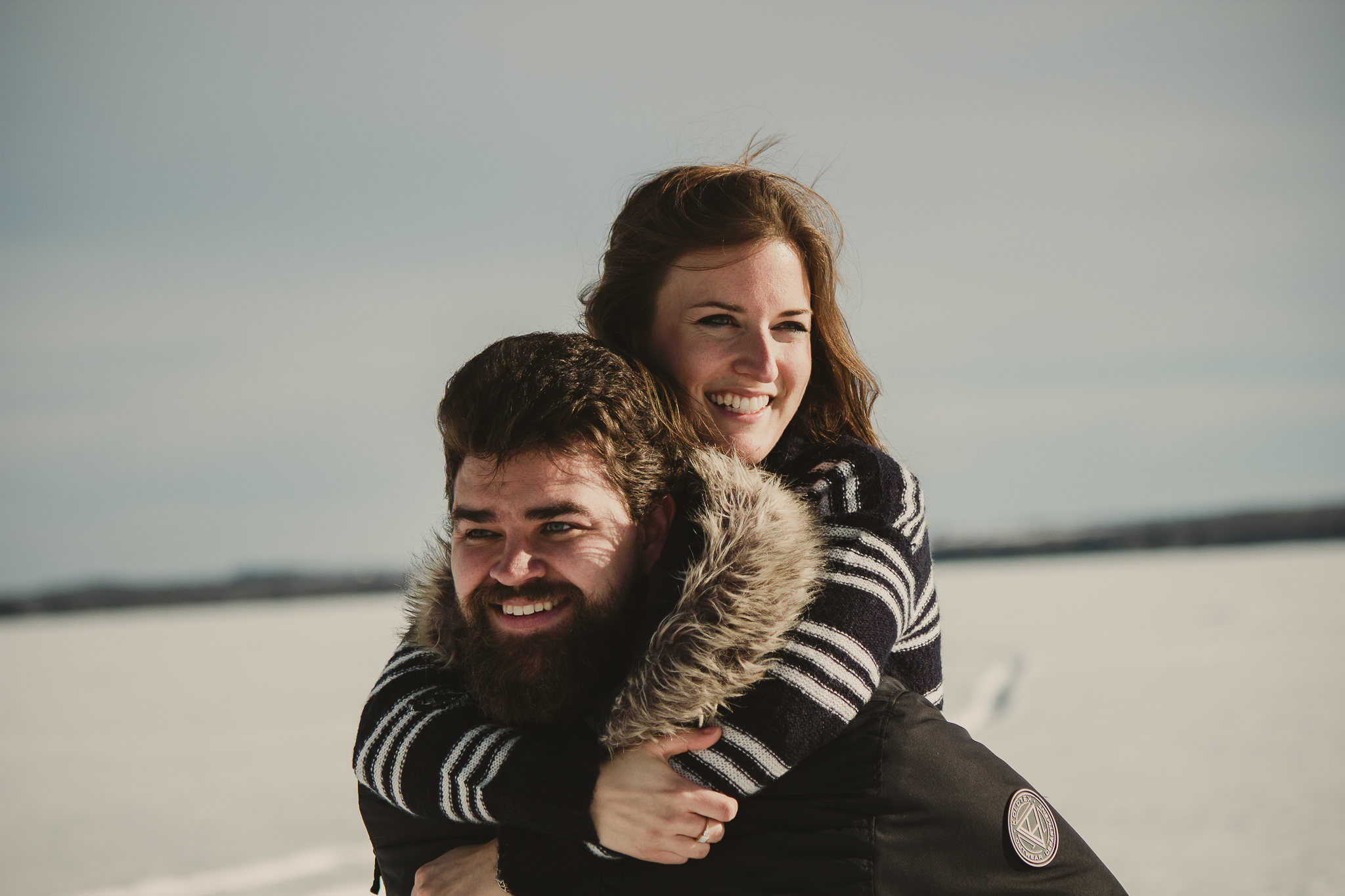 man with beard piggy backs woman in the snow