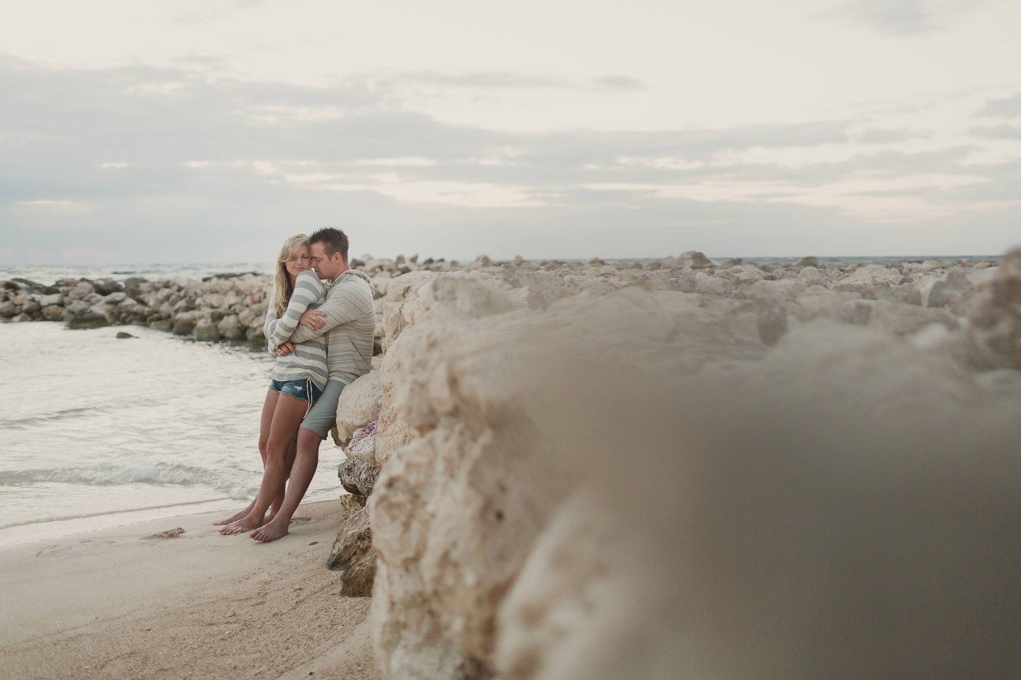 couple in an embrace leaning against a rock wall by water